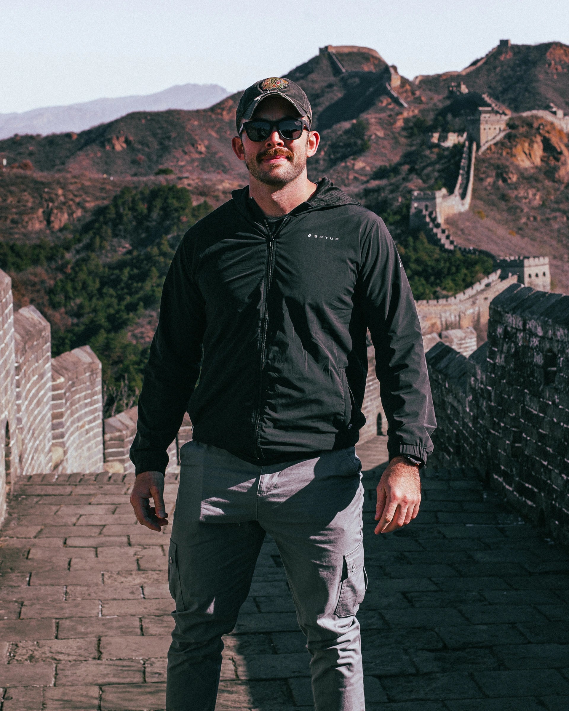 Man standing on the Great Wall of China wearing a Satus Core Jacket in black.