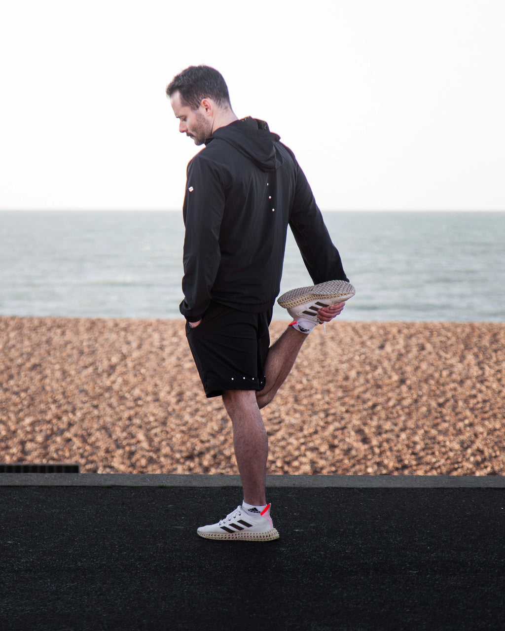 Man standing on a stretching before a run wearing a black Satus Core Jacket and Shorts