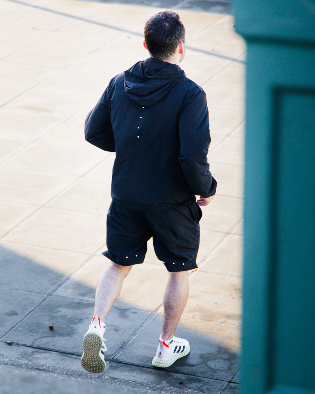 Man wearing black Satus core jacket and shorts running along a sidewalk.
