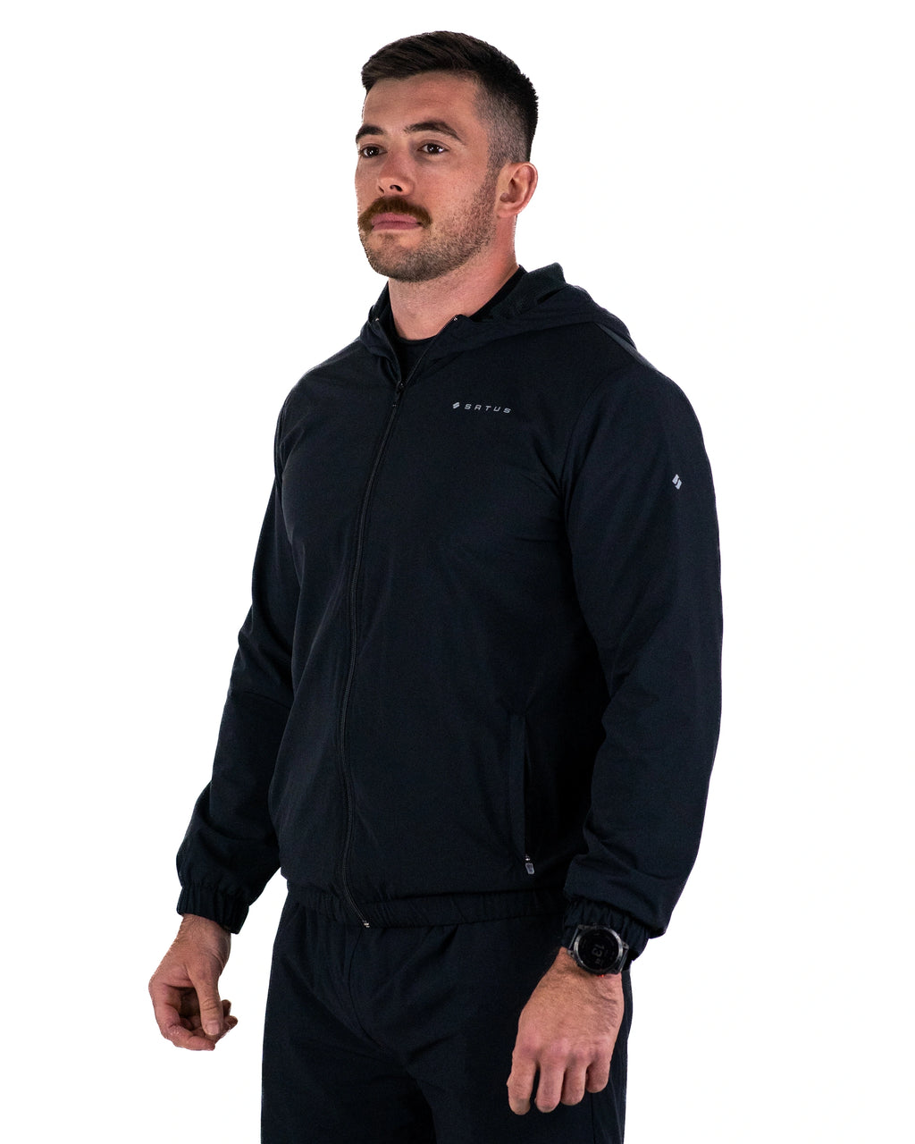 Man stood looking into the distance wearing a black Satus Core Jacket in a photo studio
