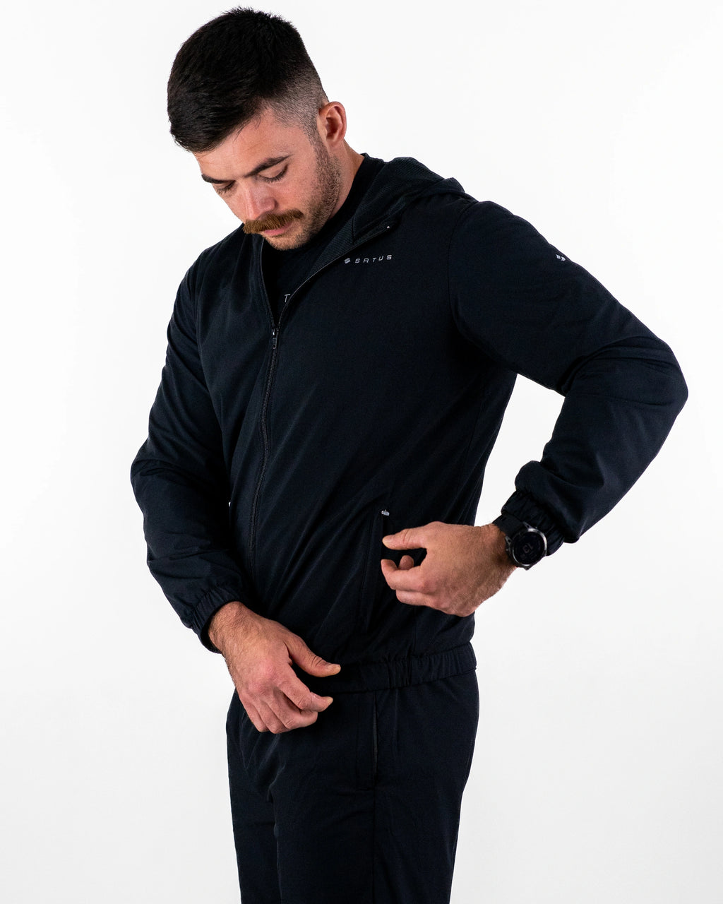 Man using zip on black Satus Core Jacket in photo studio
