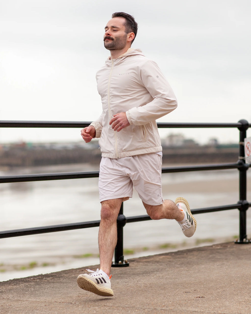 Man running outdoors on a path by a waterfront wearing tan coloured sportswear