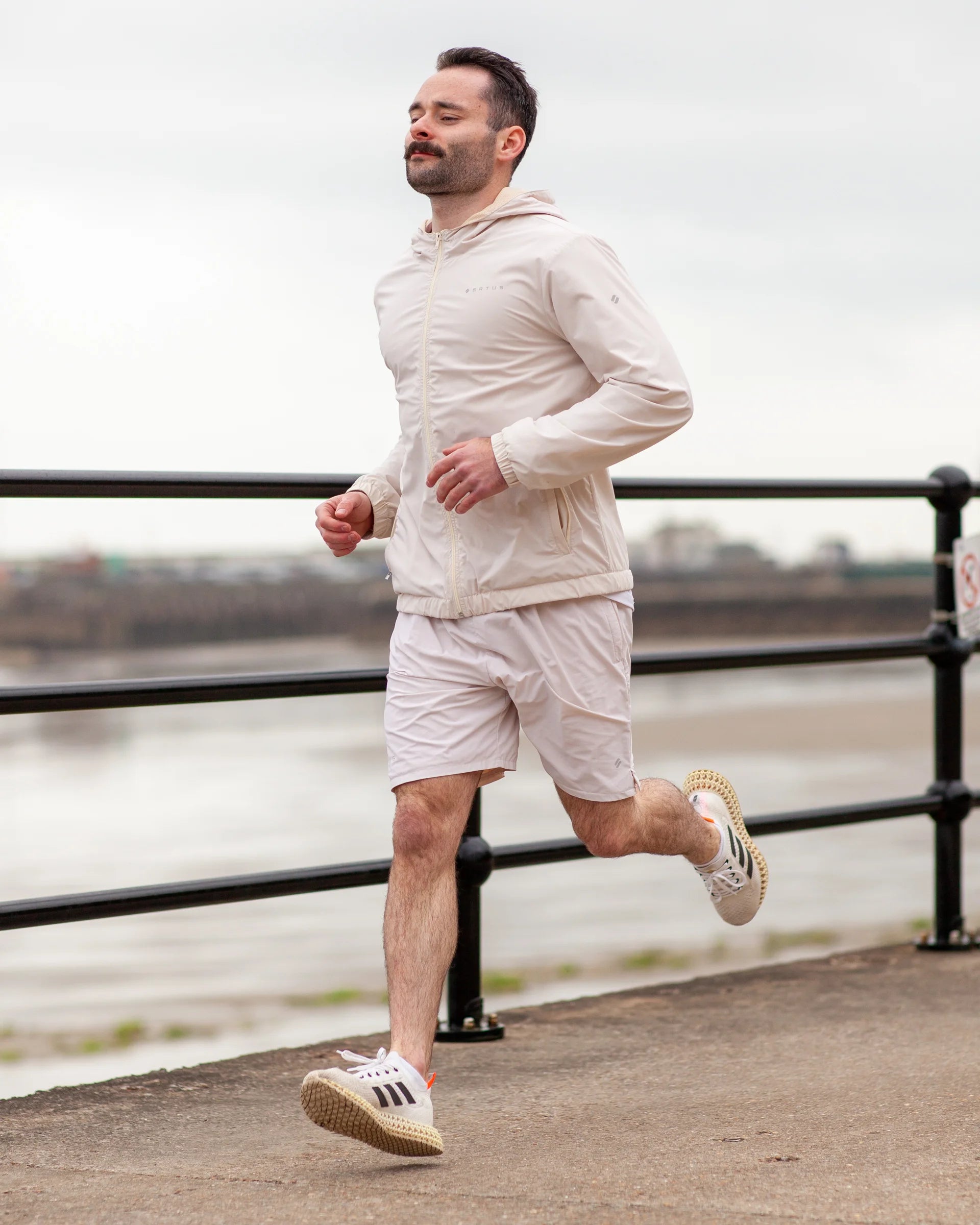 Man running outdoors on a path by a waterfront wearing tan coloured sportswear