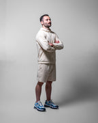 Man wearing a tan sports jacket and shorts with blue sneakers on a gray background