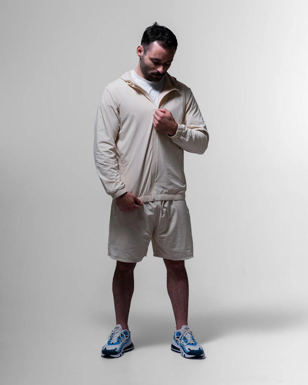 Man wearing a beige tracksuit with blue sneakers on a plain background