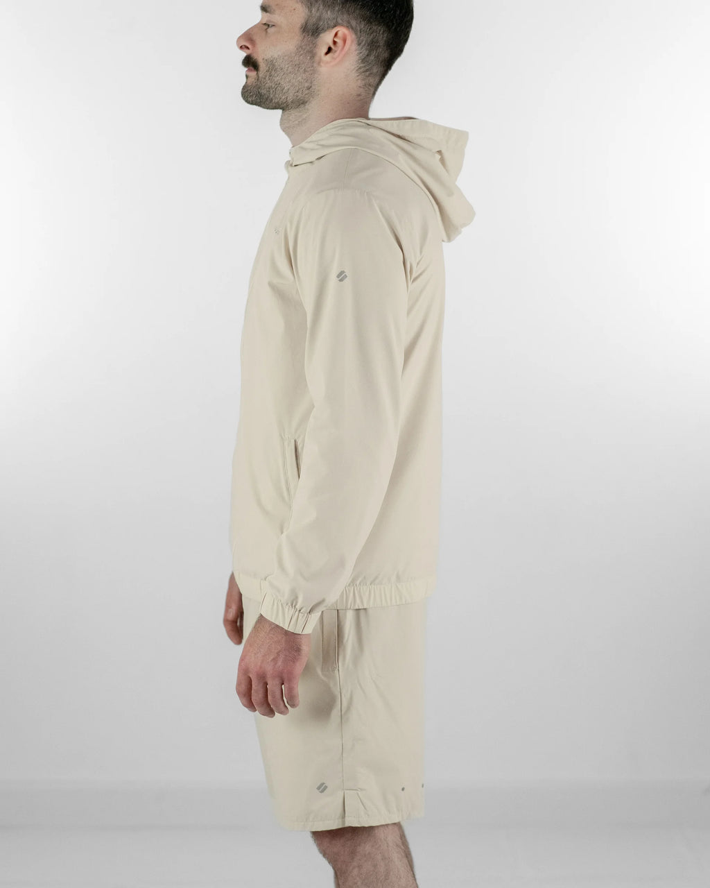 Man wearing a beige hooded jacket and shorts on a white background