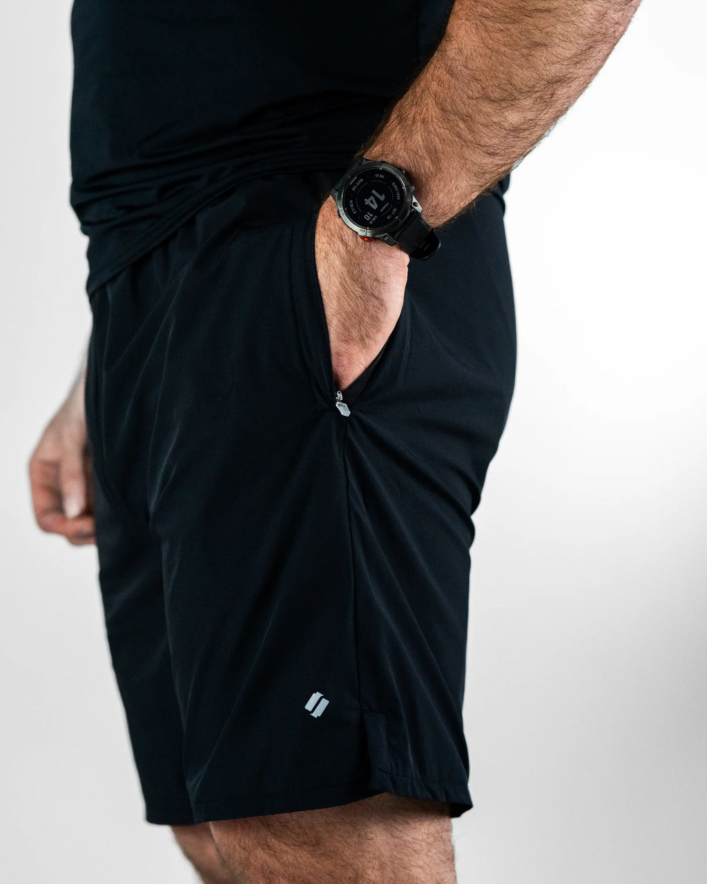 Person putting his hand in the pocket of black sports shorts with a visible brand logo on a white background