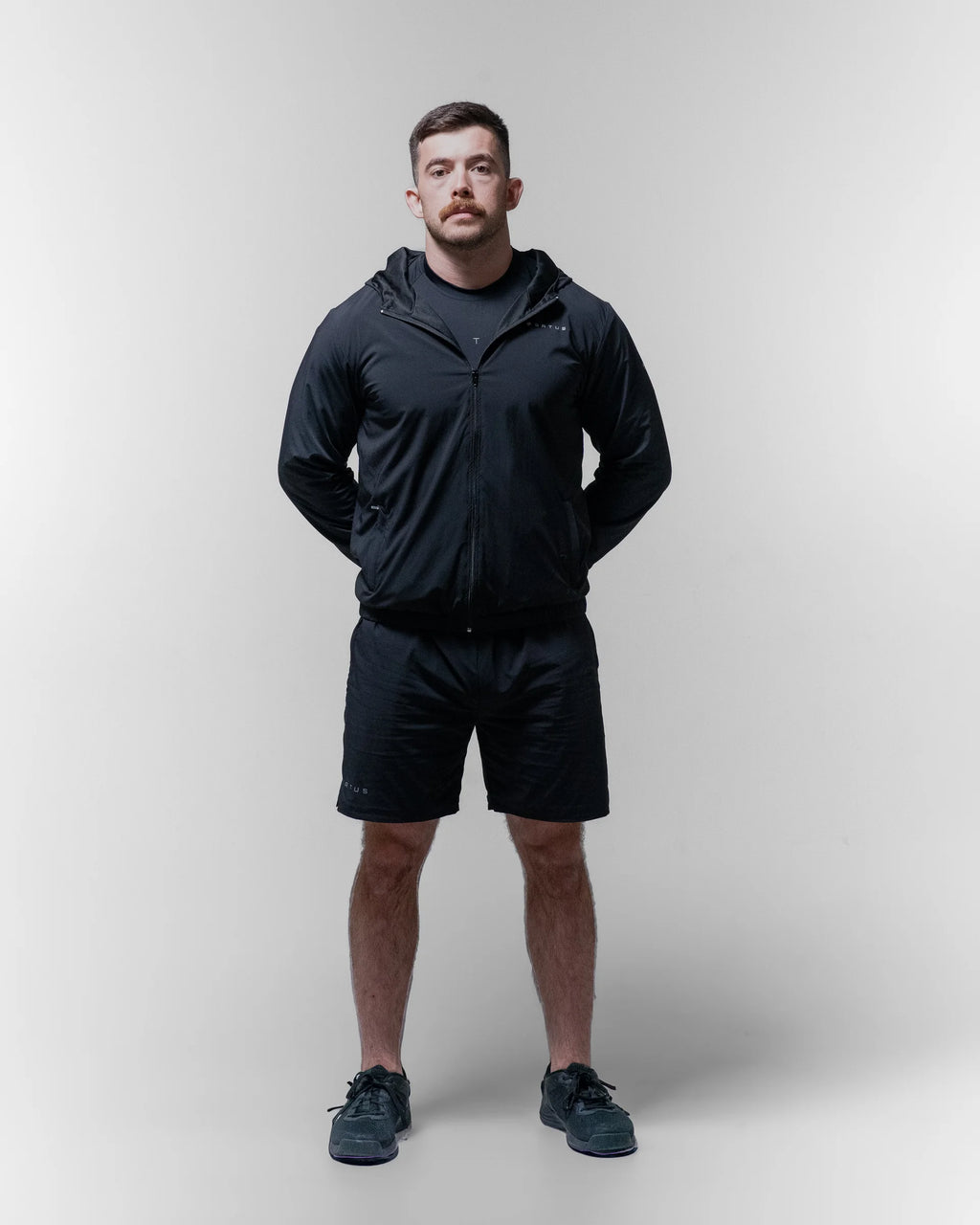 Man wearing a black sports jacket and shorts on a plain background