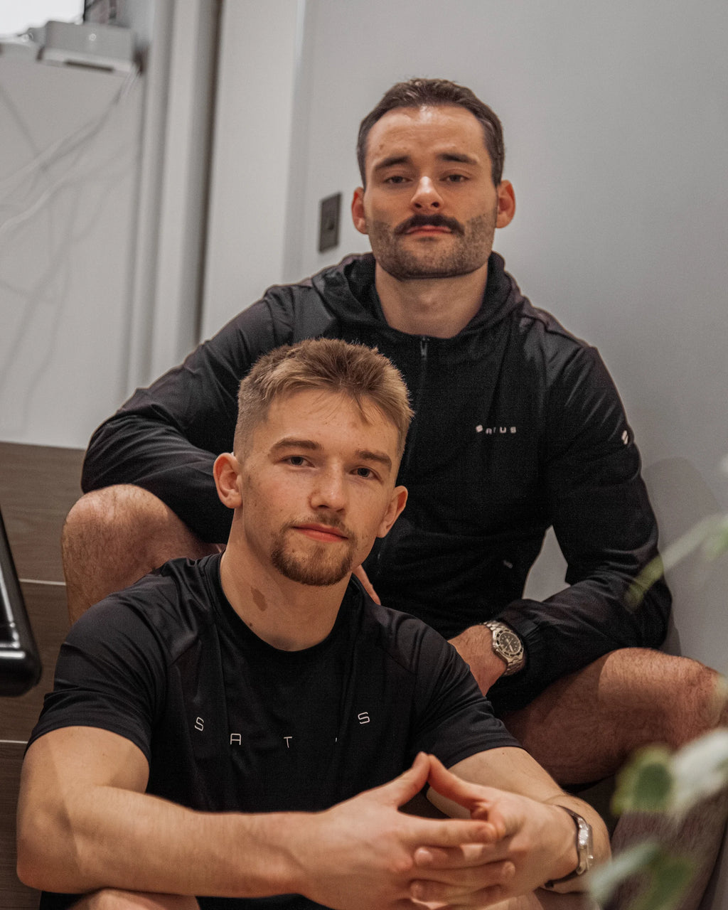 Founders of Satus sitting together in a casual setting, wearing black athletic clothing.