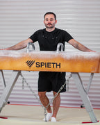 Man posing with a gymnastics pommel horse wearing a t-shirt branded "satus"