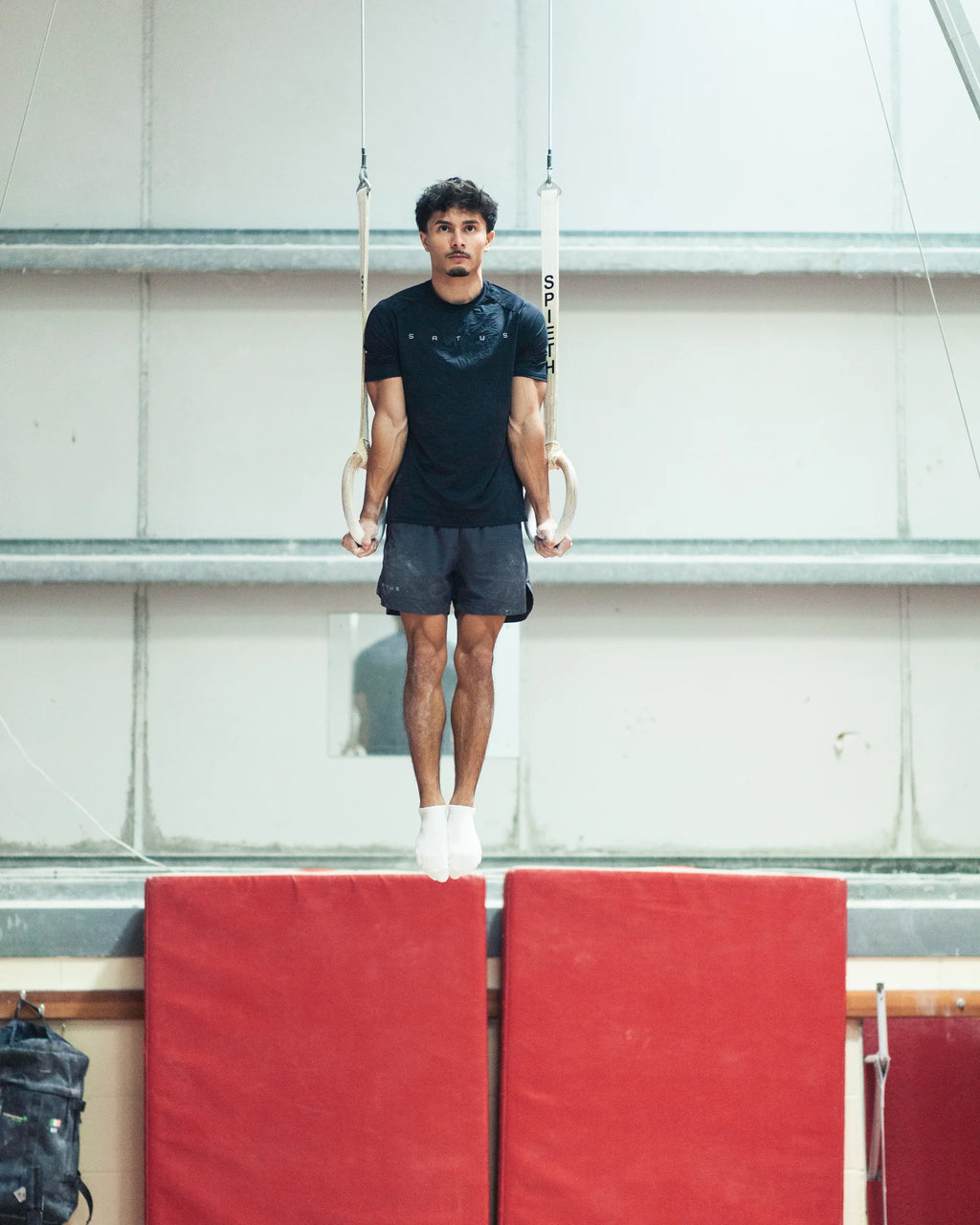 Person performing a hold on gymnastic rings with a red mat below.