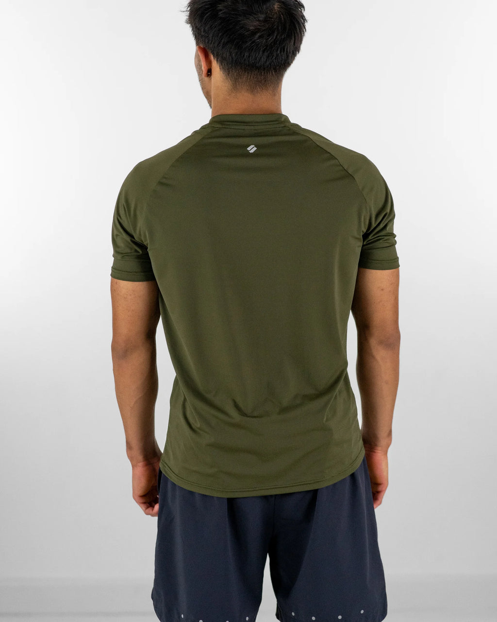Person wearing an olive green athletic shirt and grey training shorts on a white background