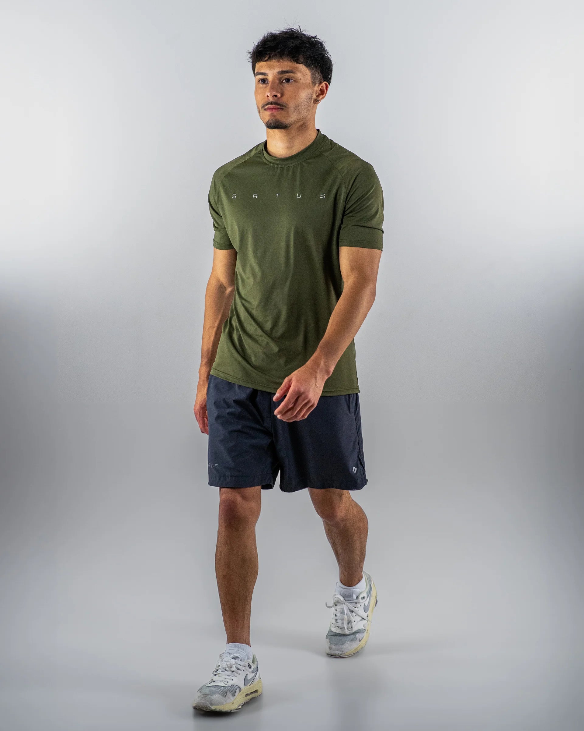 Man wearing a green athletic shirt and black shorts on a gray background