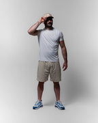 Man wearing a white sports t-shirt, beige shorts, and a cap on a plain background