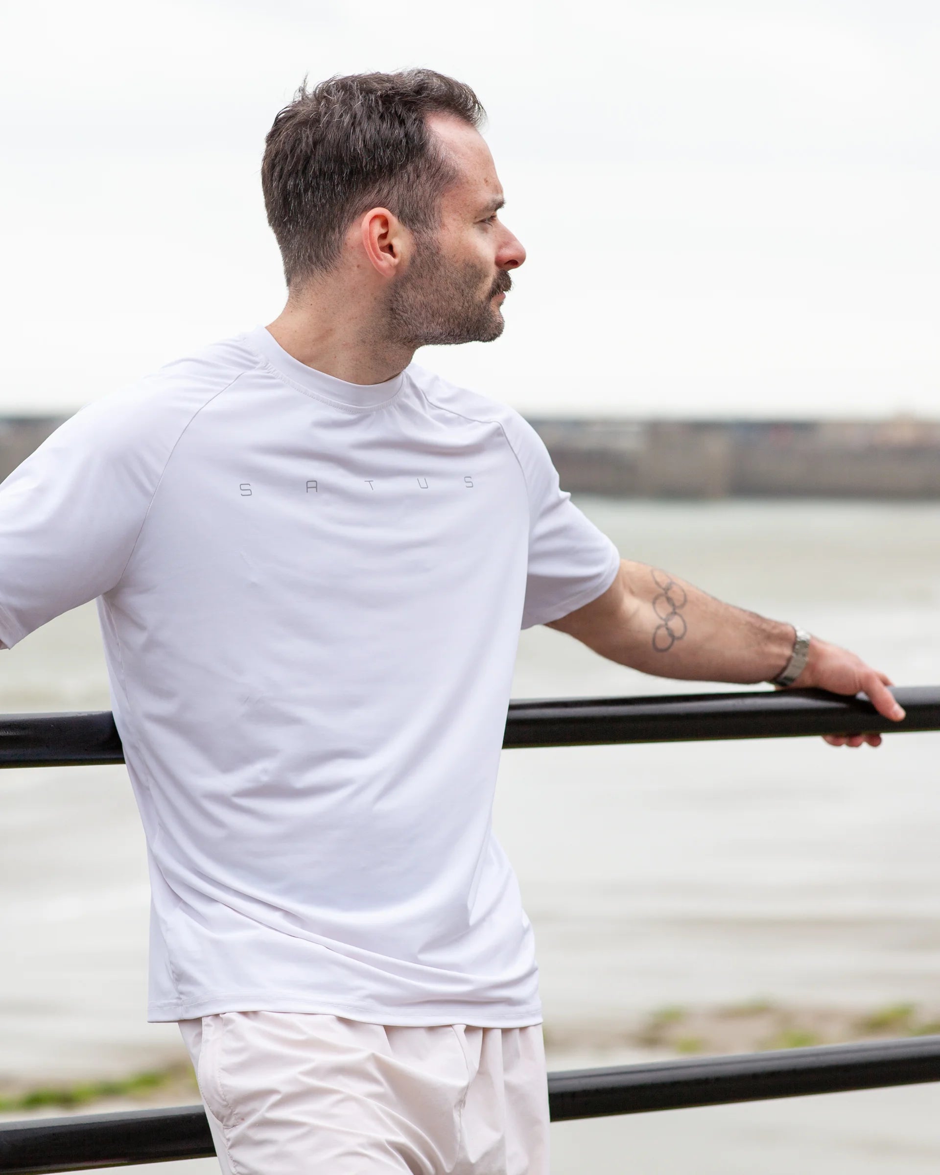 Man wearing a white sport t-shirt and pants standing by a railing with a blurred natural background