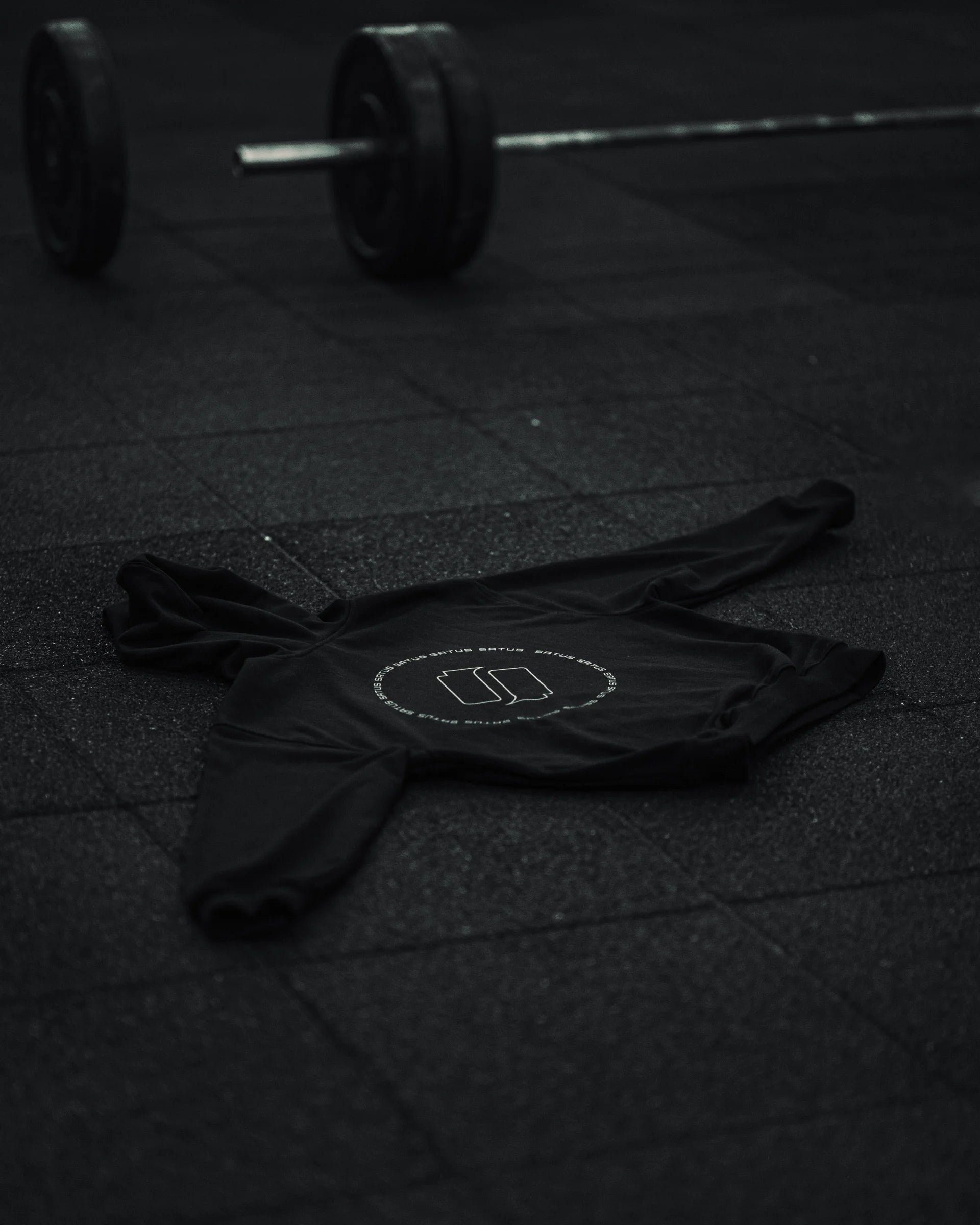 Black athletic hoodie with a logo on a dark textured surface of a gym floor.