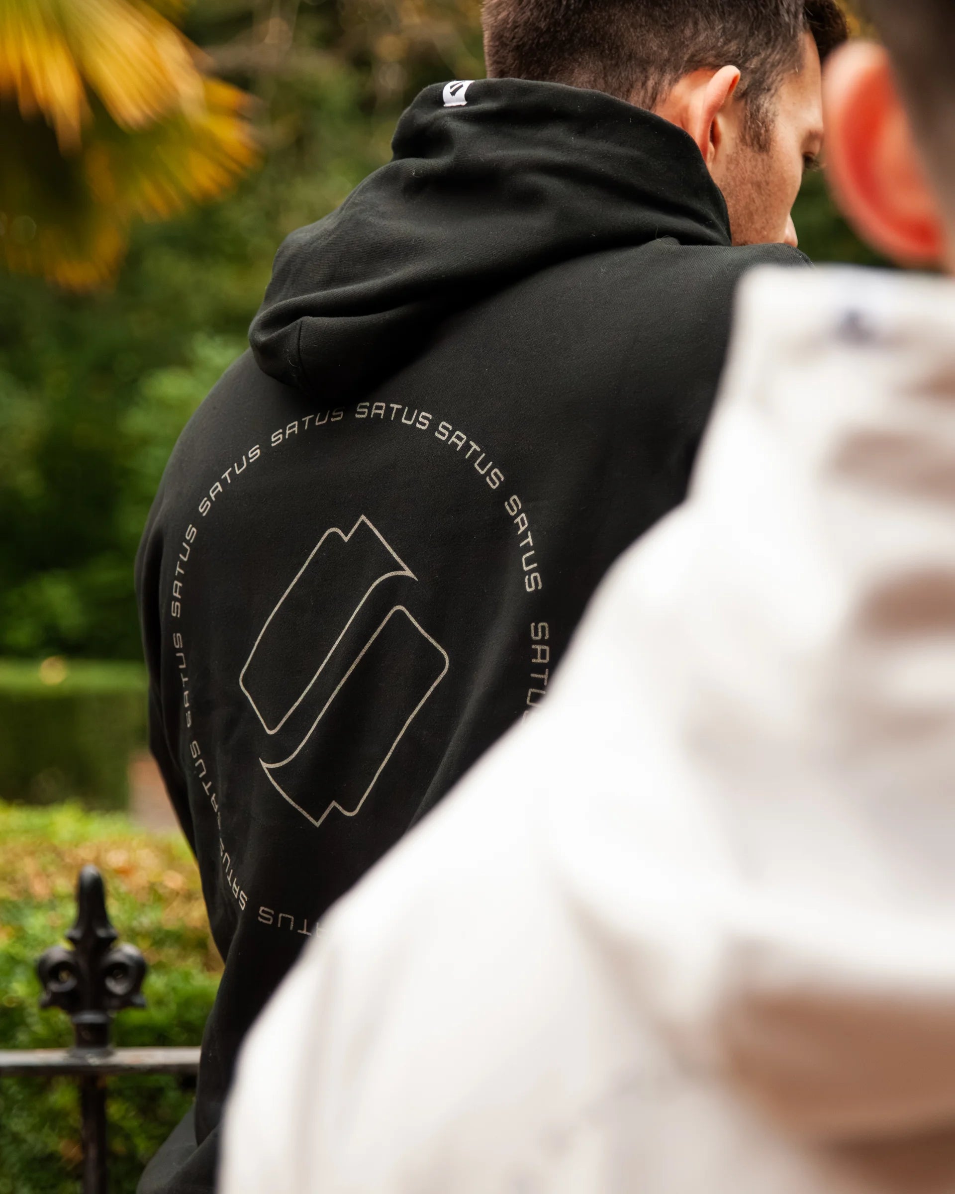 Person wearing a black hoodie with 'satus' branding, standing outdoors.