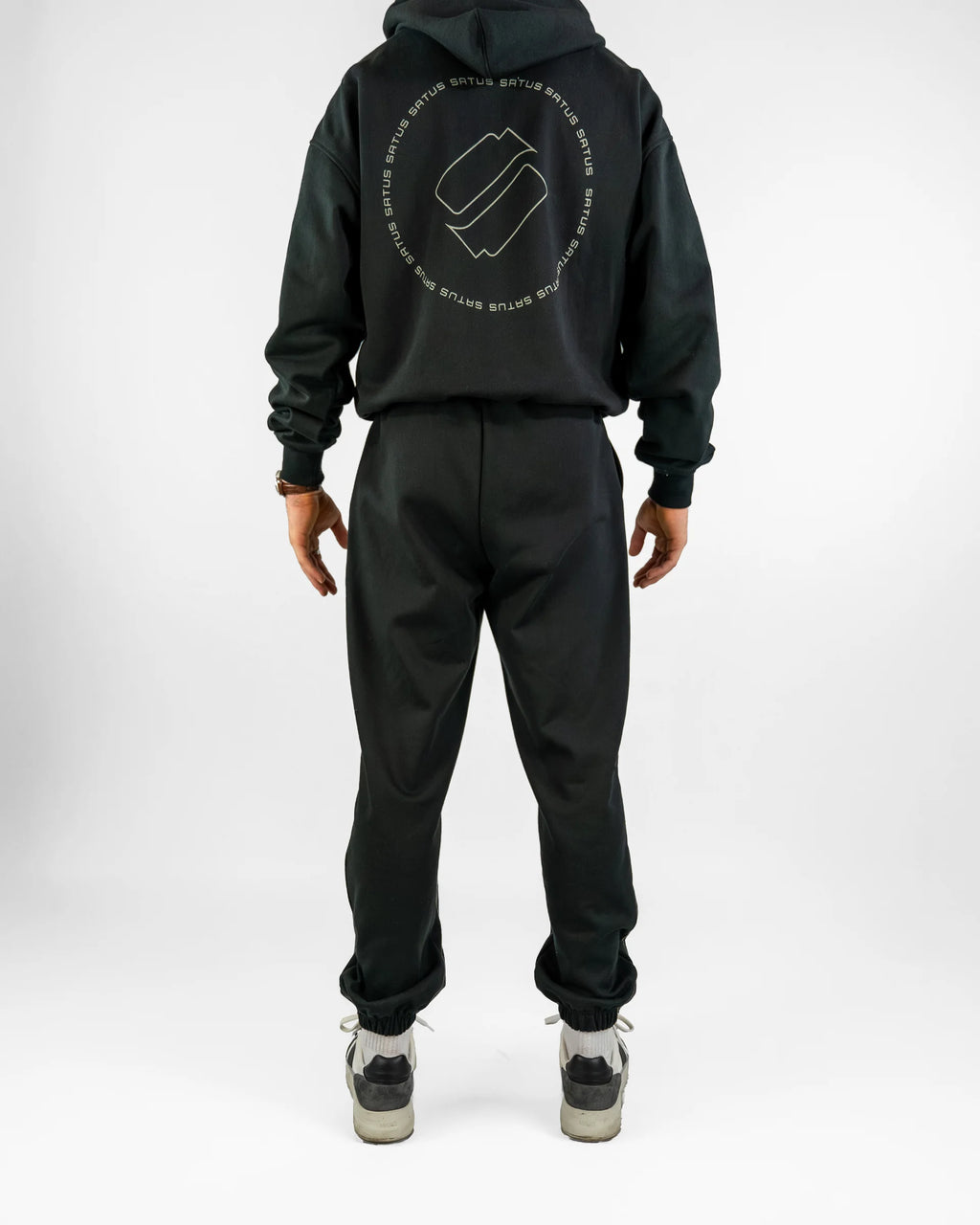 Person wearing a black hoodie and joggers set with a logo on the back, standing against a white background.