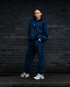 Person wearing a navy tracksuit standing against a dark brick wall.