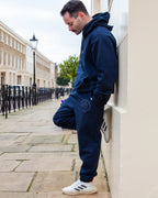 Man wearing a navy tracksuit leaning against a wall on a city street.