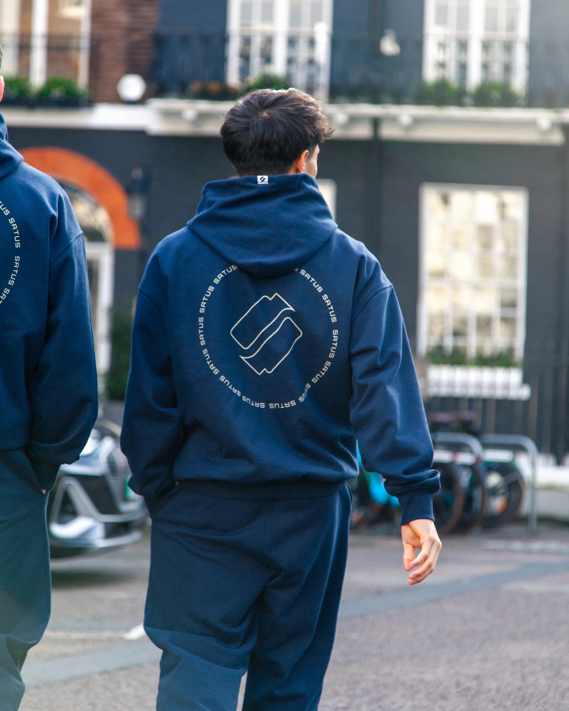 Two people wearing matching blue tracksuits with a logo on the back, walking in the city.