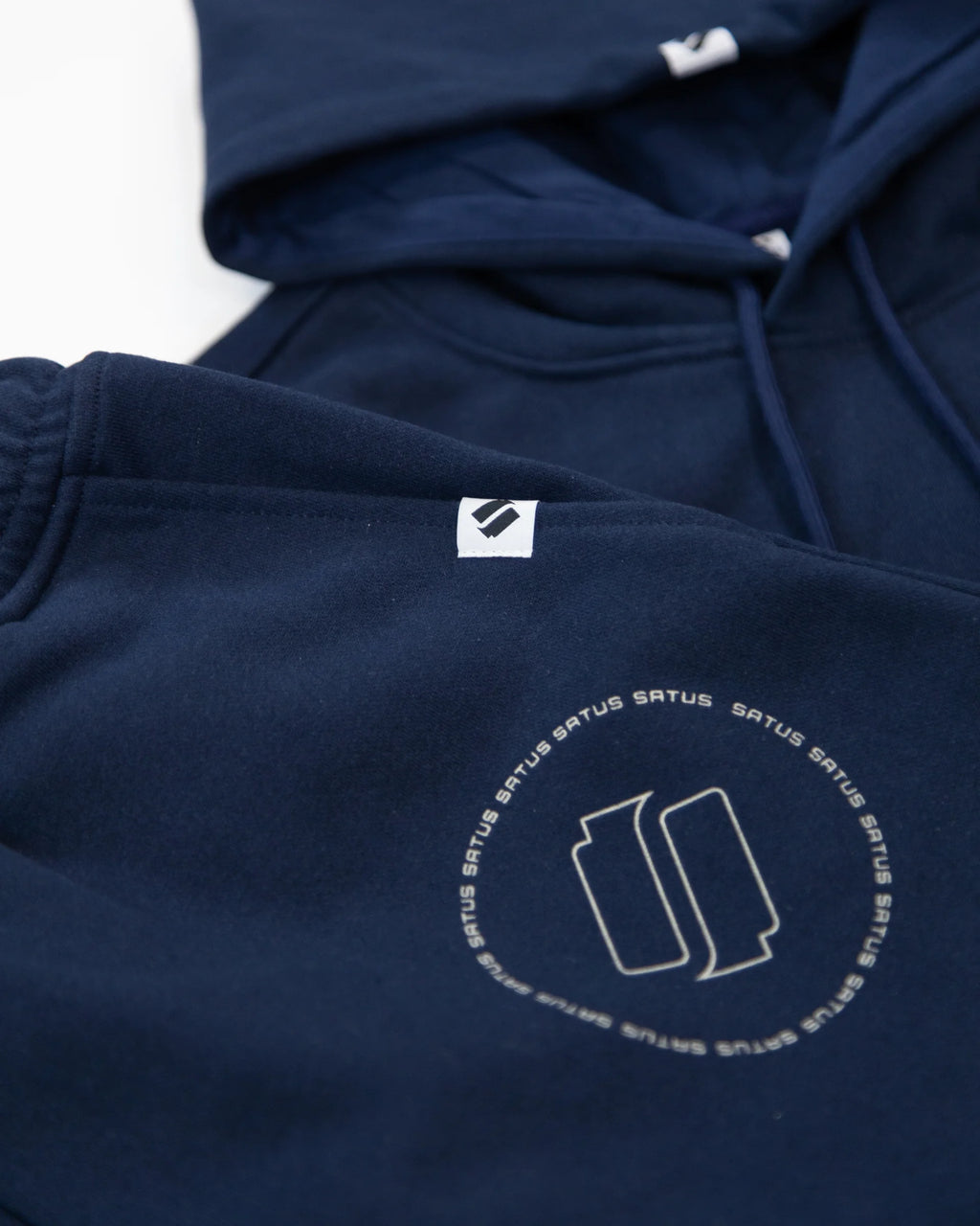Closeup of a navy blue hoodie and joggers with a 'satus' logo on a white background