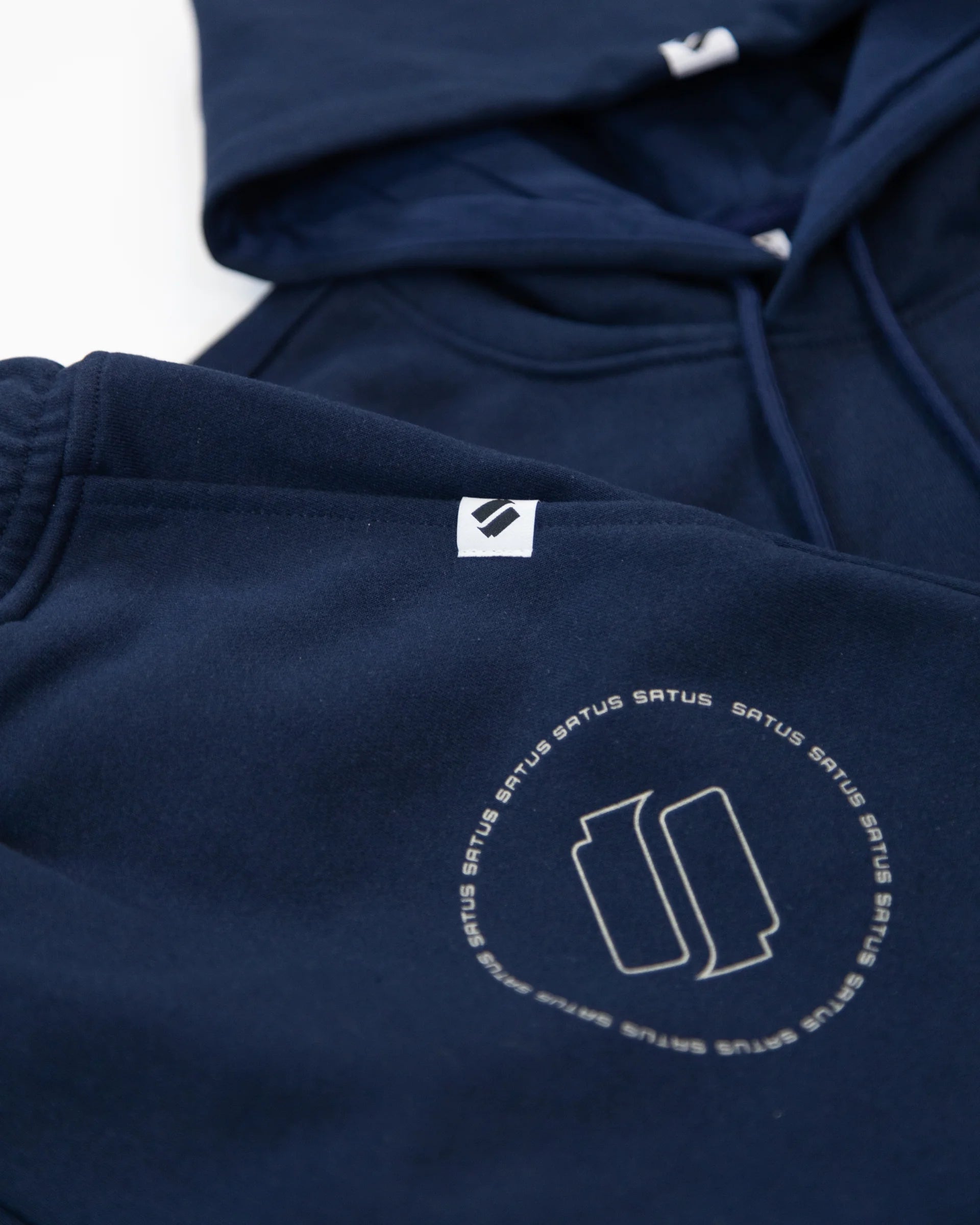 Closeup of a navy blue hoodie and joggers with a 'satus' logo on a white background