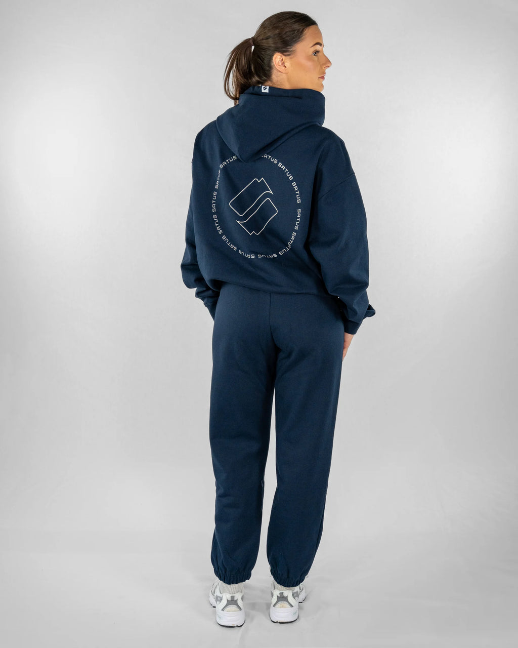 Person wearing a navy tracksuit with a logo on the back against a white background