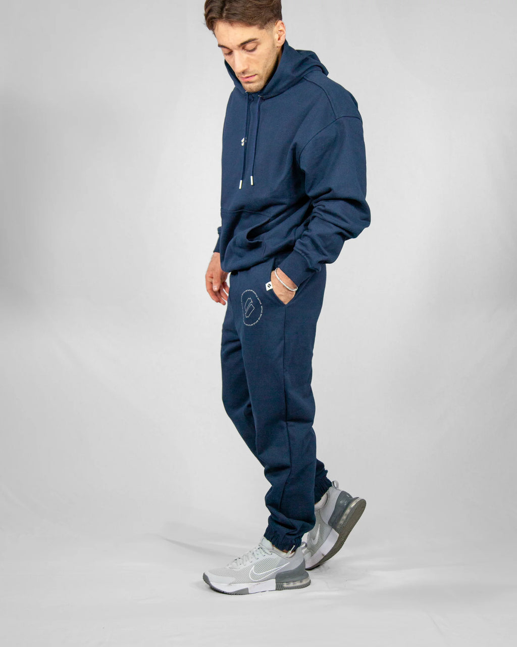 Man wearing a navy blue tracksuit with gray sneakers on a light gray background