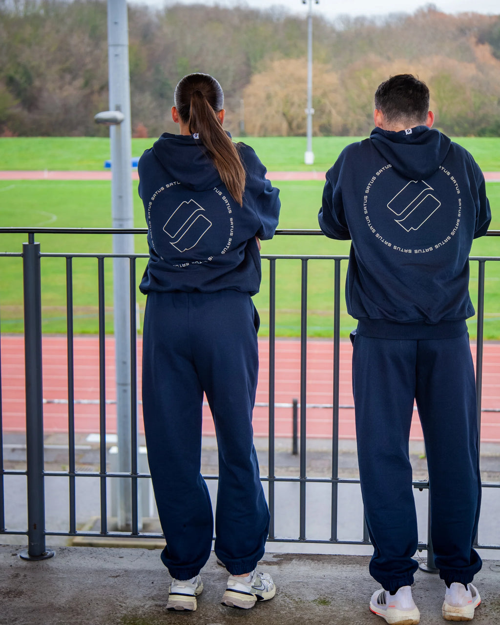 Two people wearing matching navy blue tracksuits with a logo on the back, standing on a track field.