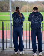 Two people wearing matching navy blue tracksuits with a logo on the back, standing on a track field.