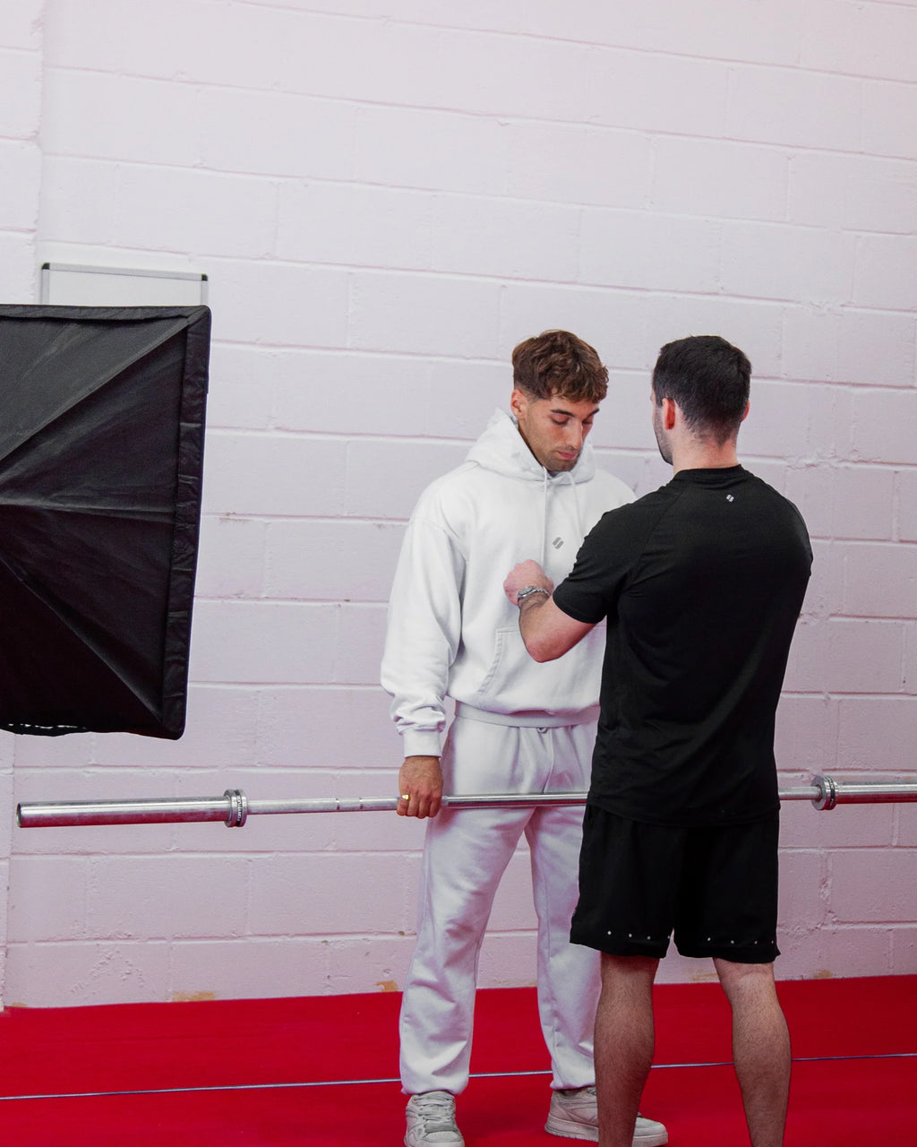 Two men in a studio setting with a light modifier and red floor, in sportswear