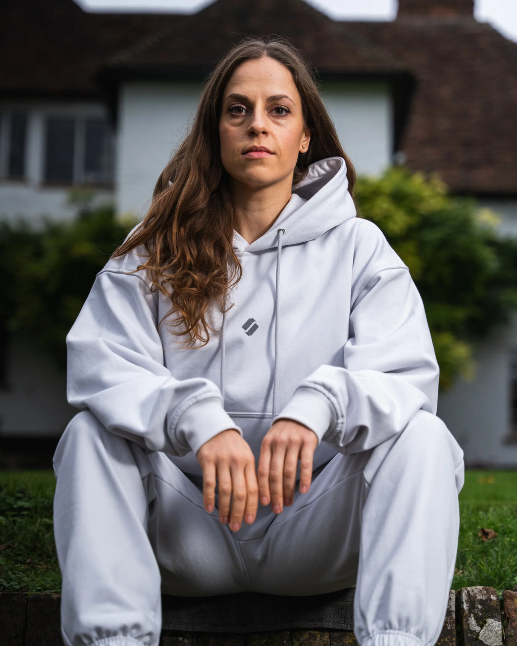 Person wearing a light gray hoodie and joggers sitting outdoors.
