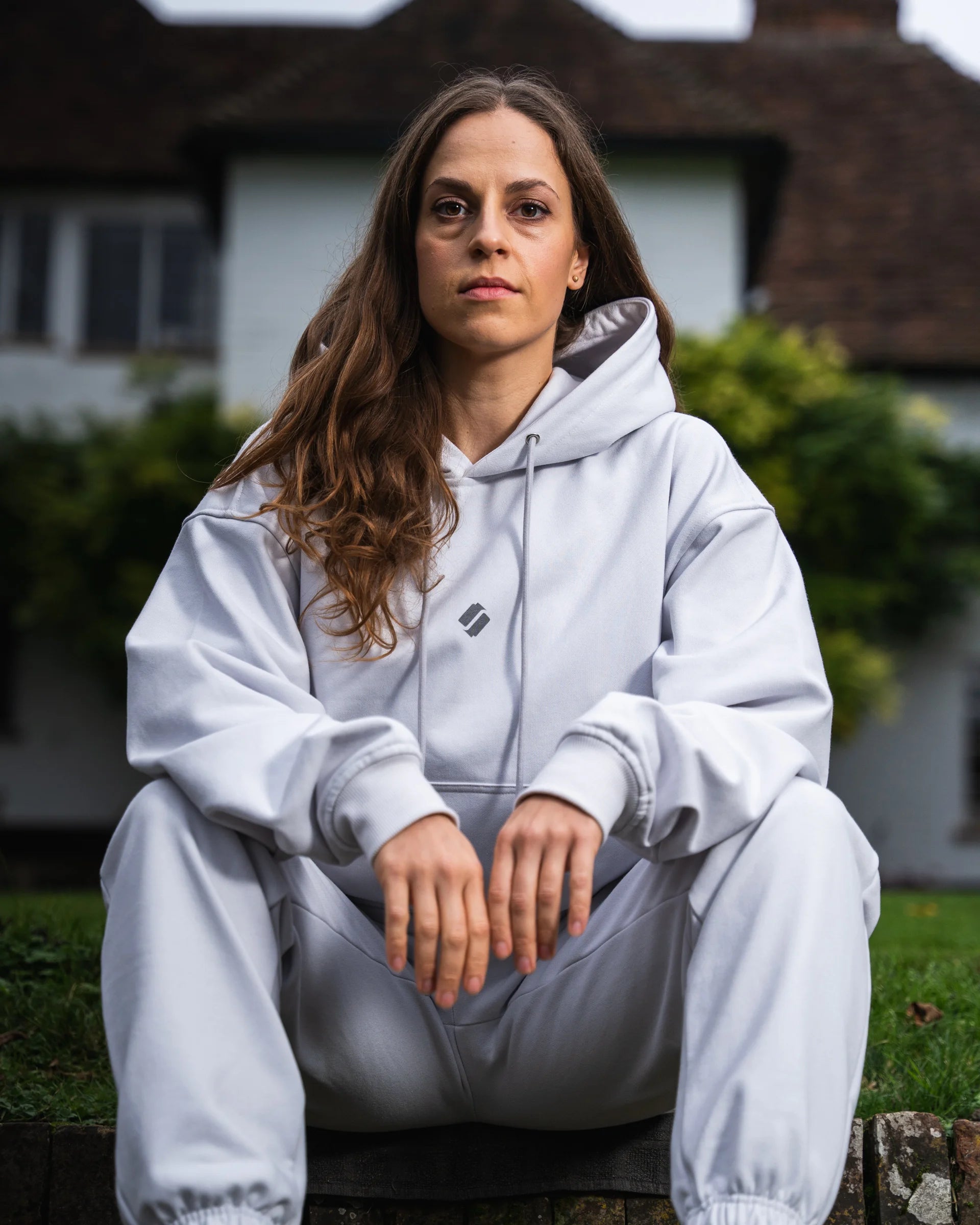 Person wearing a light gray hoodie and joggers sitting outdoors.