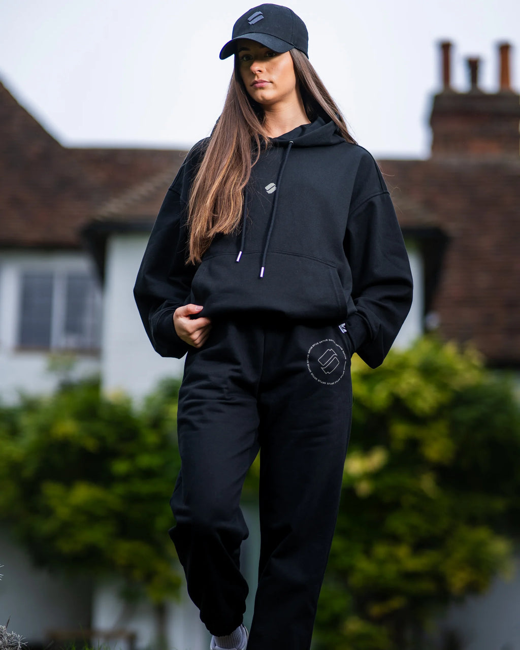 Person wearing a black tracksuit with a logo, standing outdoors.