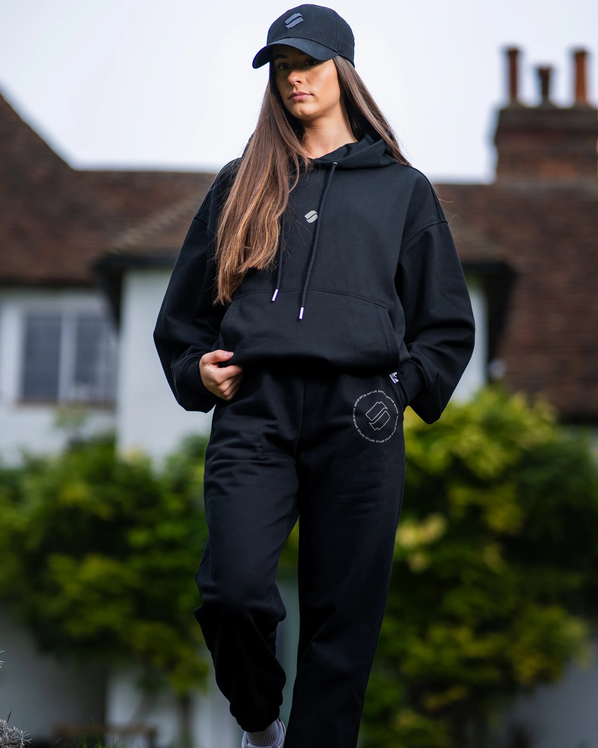 Person wearing a black tracksuit with a logo, standing outdoors.
