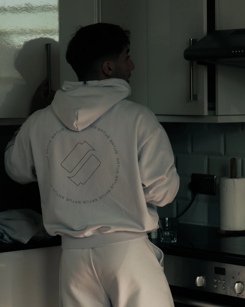 Person wearing a light gray hoodie with a logo in an aestheitc kitchen