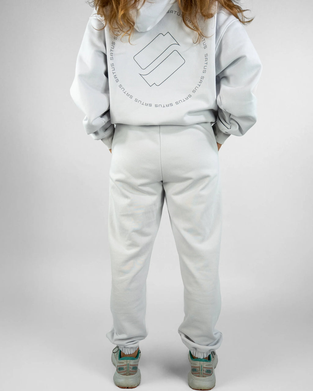 Person wearing a light gray hoodie and pants with a logo on a white background