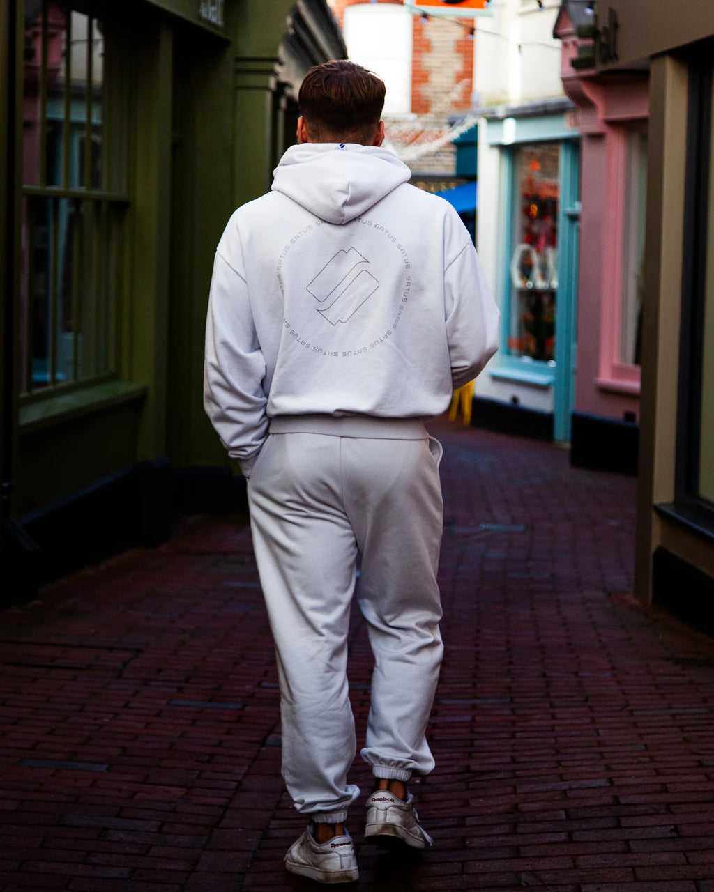Person wearing a light gray hoodie and joggers walking down an aesthetic alleyway.