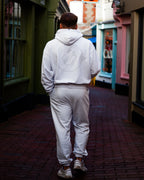 Person wearing a light gray hoodie and joggers walking down an aesthetic alleyway.