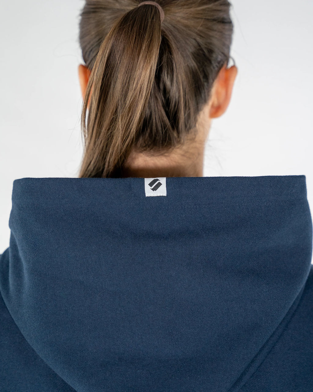 Person wearing a blue hoodie with a brand logo on the hood against a white background