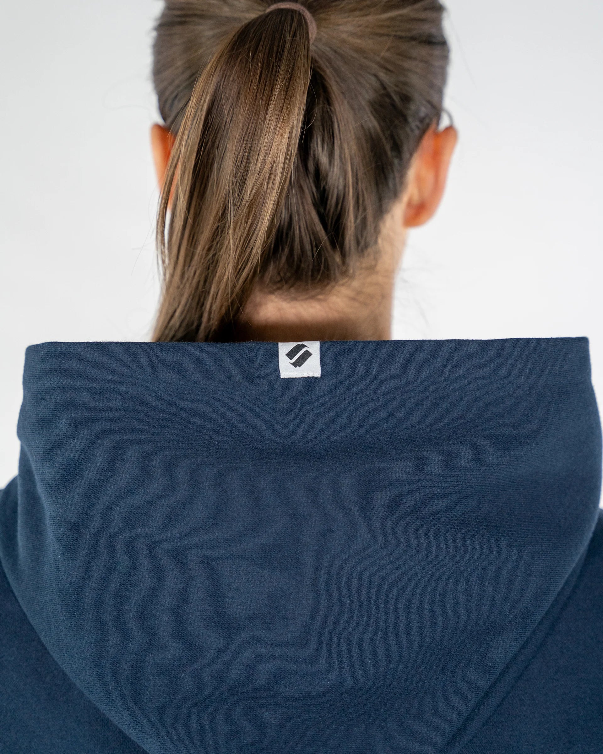 Person wearing a blue hoodie with a brand logo on the hood against a white background