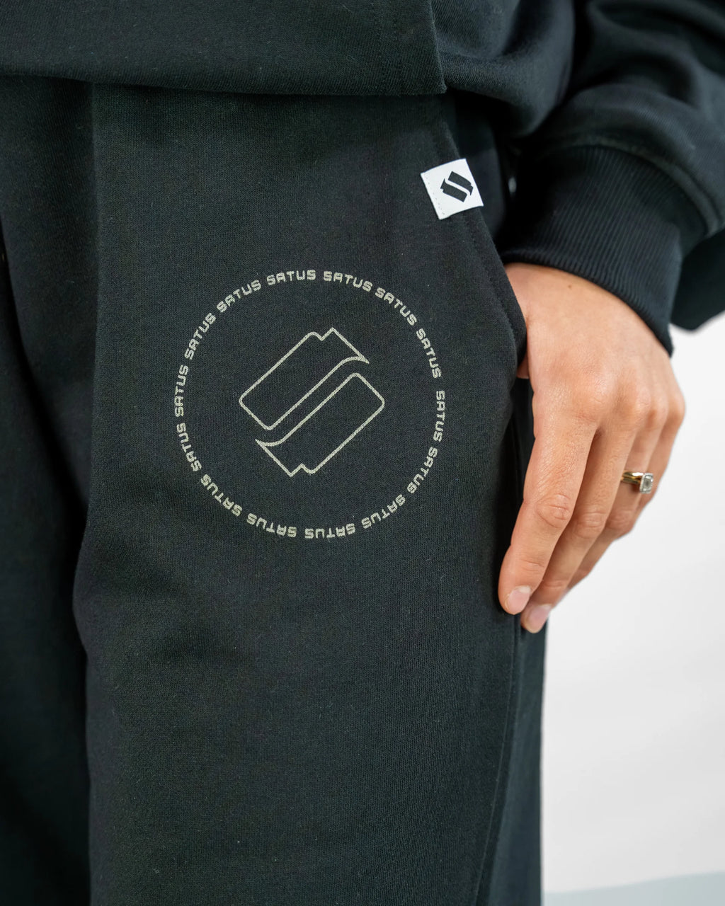 Black joggers with a logo and text on the sleeve, worn by a person.