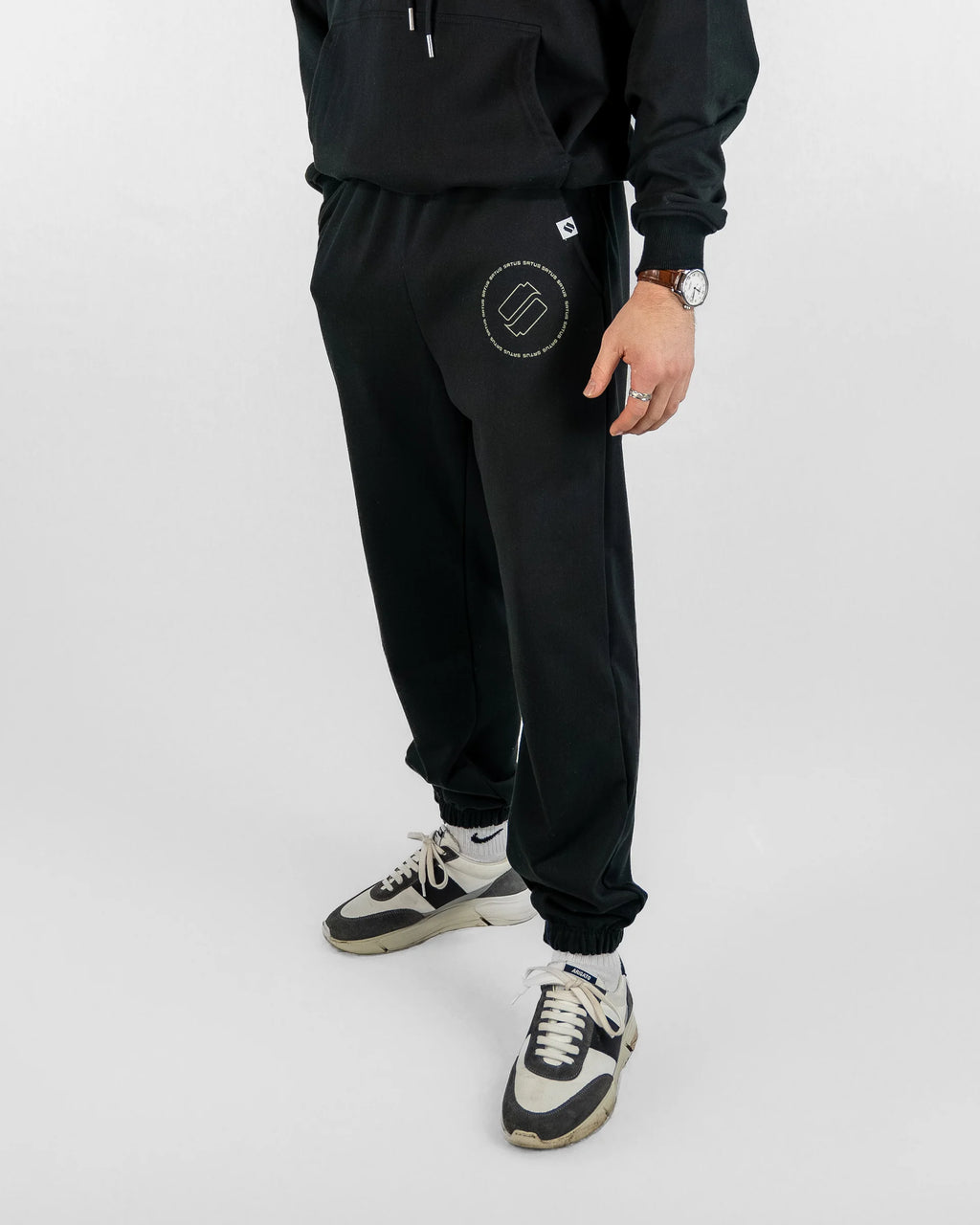 Person wearing a black tracksuit with a logo on the pants against a white background