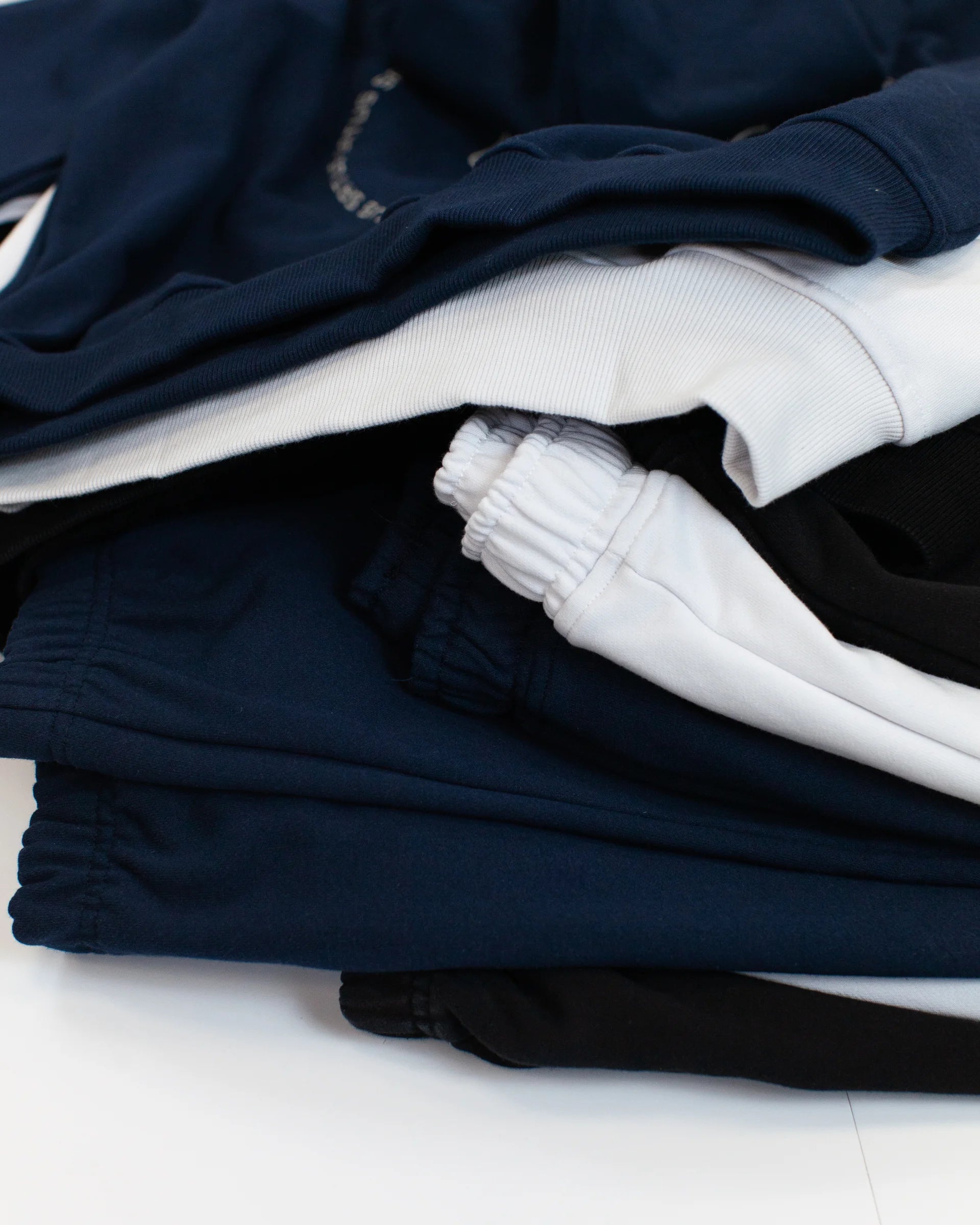 Stack of folded navy, black and white hoodies and joggers on a white surface