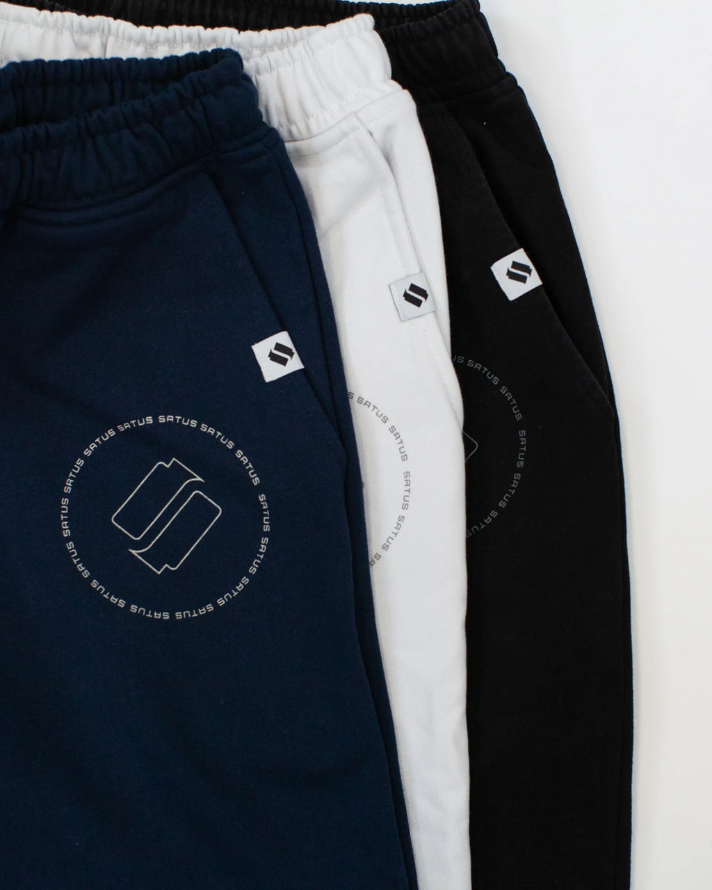 Three pairs of sweatpants in navy, white, and black with a logo on a white background.
