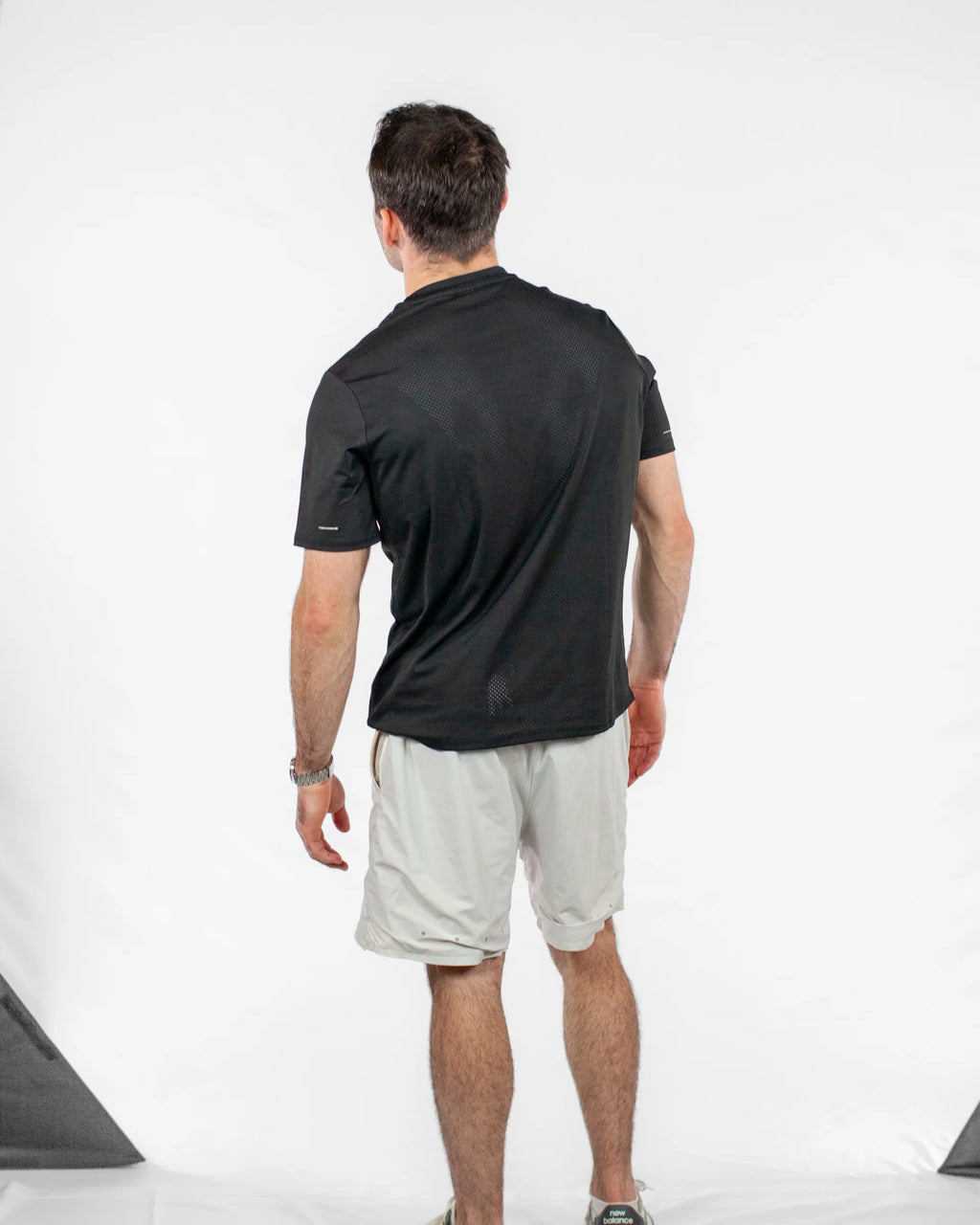 Man wearing a black shirt and light gray shorts on a white background