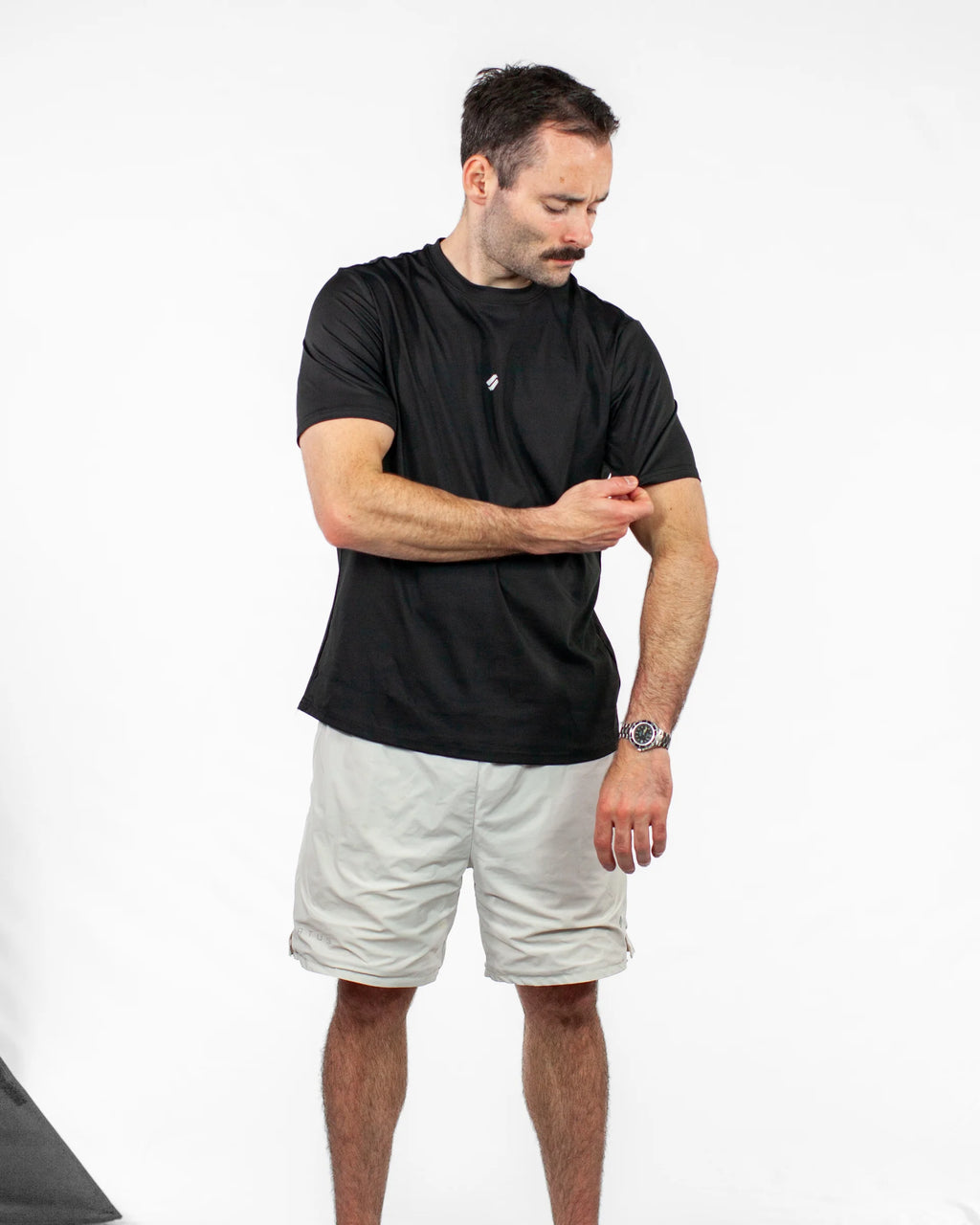 Man wearing a black t-shirt and light-colored shorts on a white background