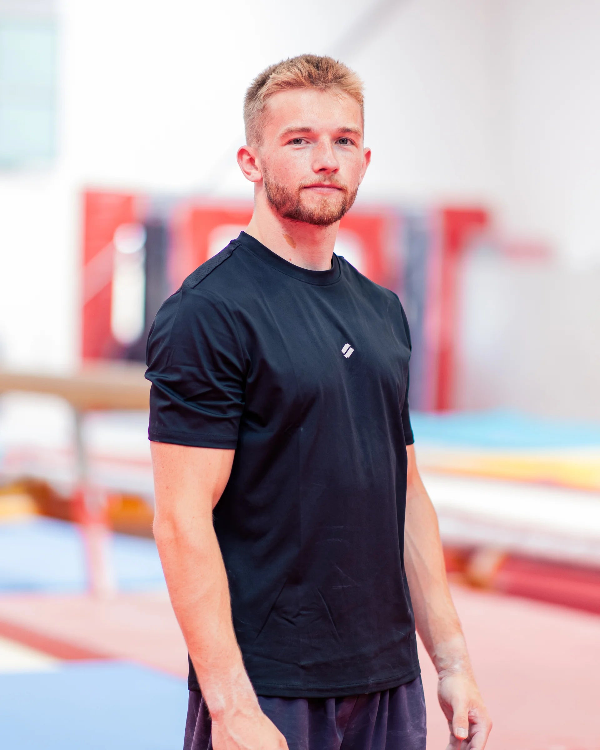 Man wearing a black t-shirt with a satus logo in an indoor gym
