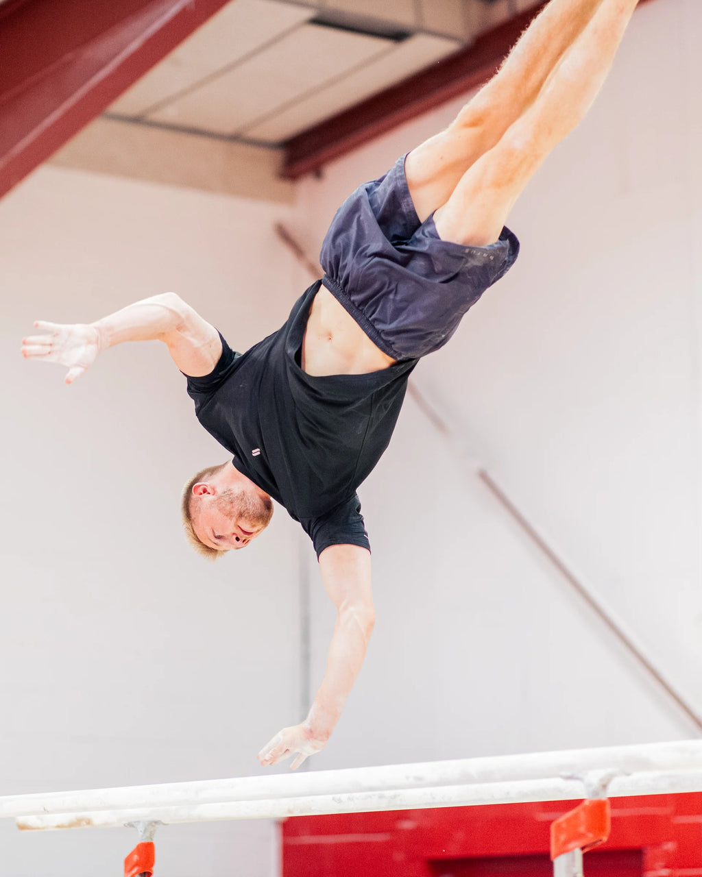 Person performing a gymnastics skill on the parallel bars wearing sports t-shirt and training shorts.